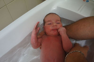 Cropped hand of man bathing baby boy in bathtub