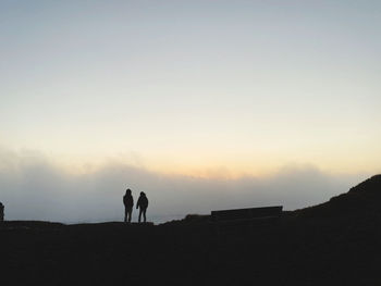 Silhouette men standing on land against sky during sunset