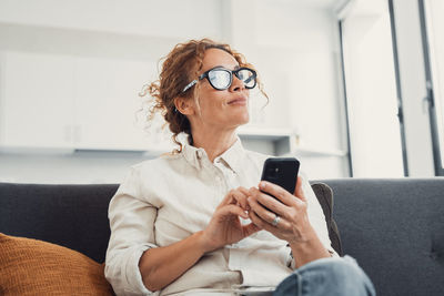 Young woman using phone while sitting on sofa at home