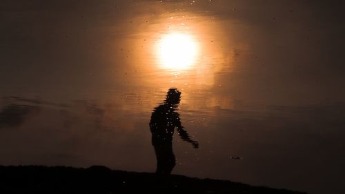 Silhouette man standing in water against sky during sunset