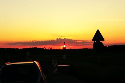 Silhouette car against orange sky during sunset