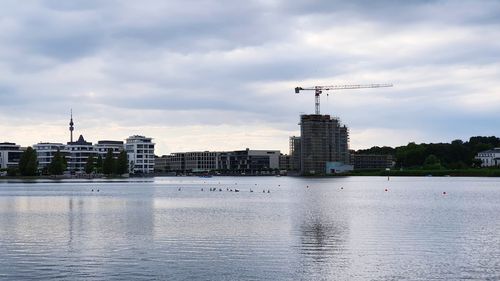 View of buildings by river against cloudy sky