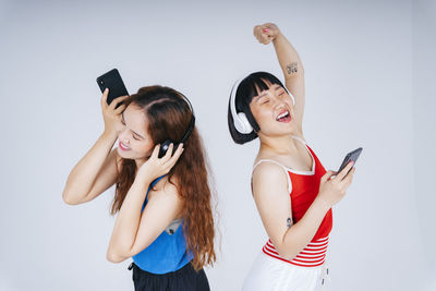 Lesbian couple using phone while listening music against gray background