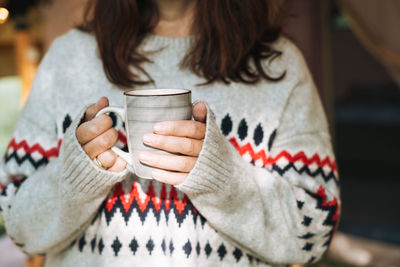 Brunette woman in nordic sweater drinking tea and relaxing in glamping in nature