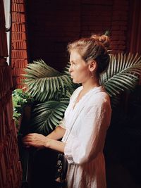 Young woman looking away while standing against plants