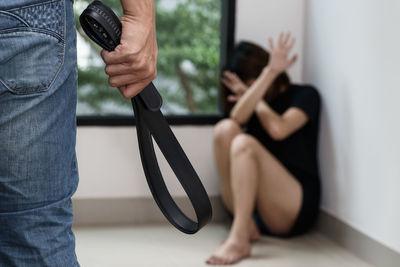 Midsection of man holding belt with woman sitting in corner