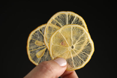 Close-up of hand holding banana against black background