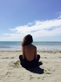 Rear view of woman sitting at beach against sky