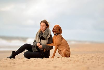 Full length of woman with dog sitting on sand at beach