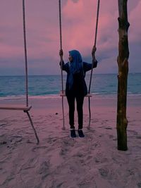 Full length of woman swinging at beach against sky during sunset