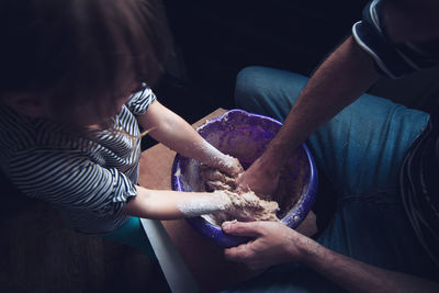 High angle view of father and daughter making dough in container on table