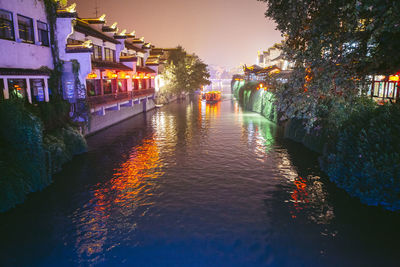 Boat on canal amidst illuminated buildings in city at dusk