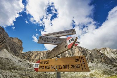 Low angle view of directional signs against rocky mountains at alto adige