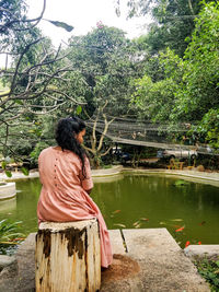 Rear view of woman standing by lake against trees