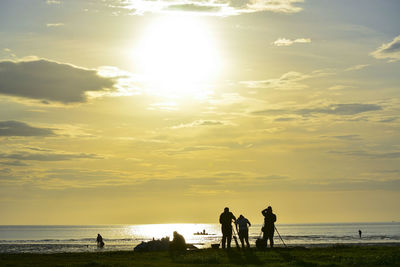 Silhouette people on beach against sky during sunset