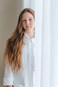 Portrait of young woman standing by window