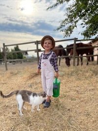 Portrait of cute toddler in a lanscape with horses and a cat