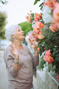 Elderly woman admiring beautiful bushes with colorful roses