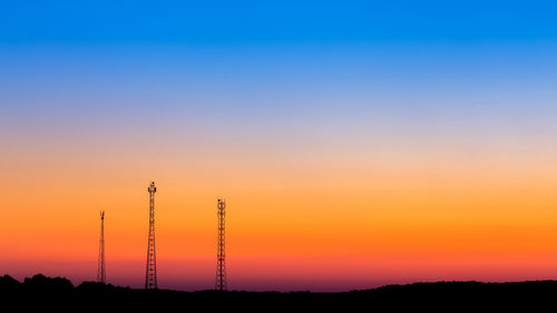 Three high telecommunication towers silhouette on horizon with gradient blue to orange dusk sky