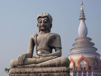 Low angle view of buddha statue by temple against clear sky