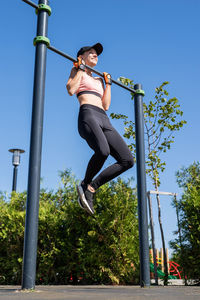 Woman in sportclothes working out on the sports ground in sunny summer day, doing pull ups
