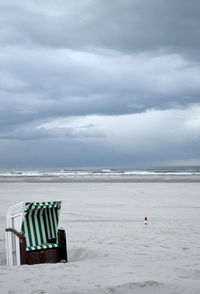 Hooded chair at beach against cloudy sky