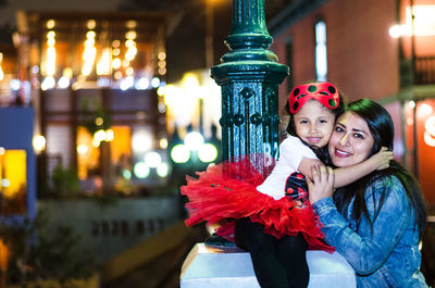 Portrait of smiling mother and daughter embracing by pole at night