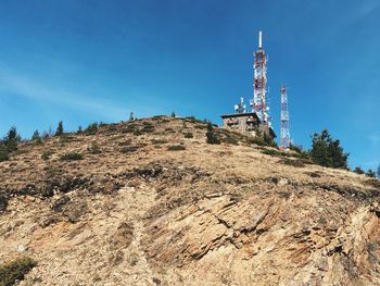 Low angle view of repeater towers on mountain against sky