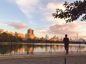 Rear view of man standing by river in city against sky