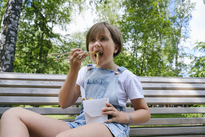 Teenage girl on a walk on a summer day in the park has lunch with noodles wok