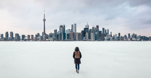 Rear view of woman walking on frozen lake ontario with financial district in background