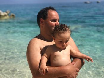 Father carrying son while standing against sea