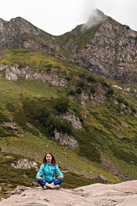 Meditating young woman in blue sitting on stone in mountain, meditation in nature, consciousness