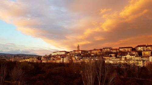 Illuminated buildings in town against sky at sunset