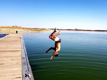 Full length of shirtless man jumping in lake against clear sky