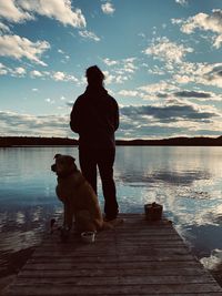 Rear view of man with dog on pier against sky