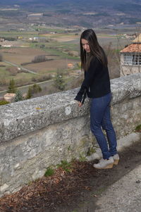 Side view of young woman standing by retaining wall on observation point