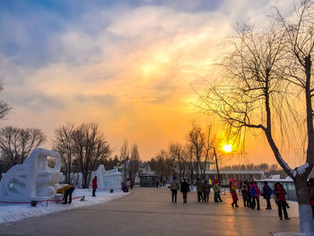 People on snow covered landscape against sky during sunset