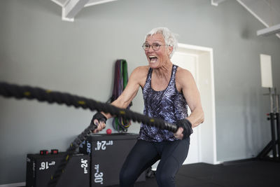 Active senior woman screaming while exercising with ropes at health club
