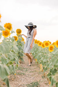 Woman standing by sunflowers on field against sky