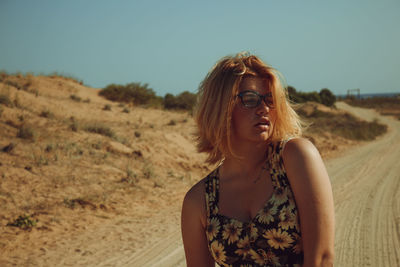 Portrait of young woman looking away while standing on land against sky