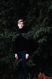 Portrait of young man standing against trees in forest