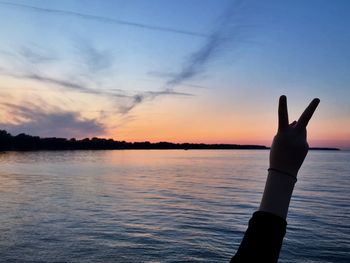 Silhouette hand against sea during sunset