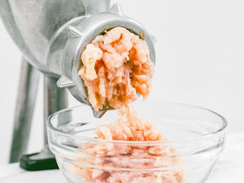 Manual meat grinder with minced meat in a glass dish on a marble table