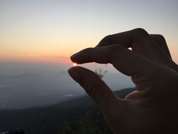Cropped hand against orange sky during sunset