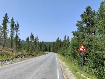 Road sign by trees against sky