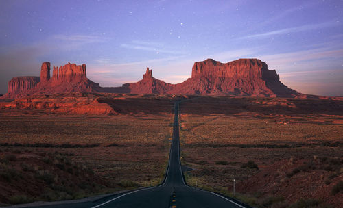 Road amidst field at desert during sunset