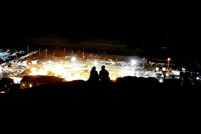 Silhouette people standing in front of sea at night
