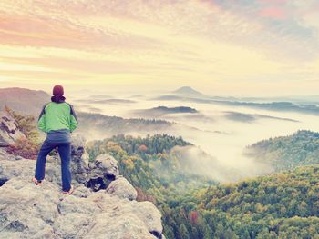 Man stay on rocky peak within daybreak and watch over misty landscape. beautiful autumn morning.