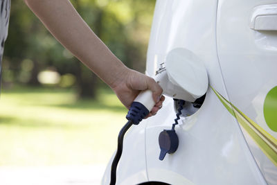 Cropped hand of person charging white electric car